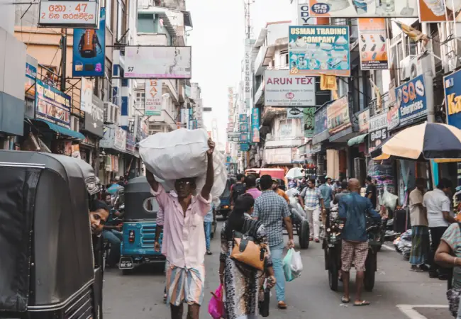 Man carrying a full sack on his head walking through a crowded street in Colombo, Sri Lanka