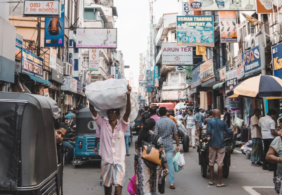 Man carrying a full sack on his head walking through a crowded street in Colombo, Sri Lanka