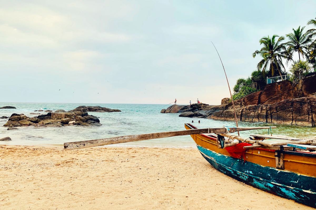 Beach in Sri Lanka with boat and people fishing on rocks in the distance